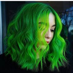 a woman with bright green hair is looking at her cell phone while she's wearing a black shirt