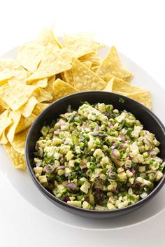 a black bowl filled with corn and salsa next to tortilla chips on a white plate