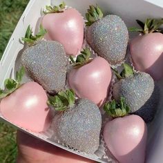 a person holding a box full of glittered strawberries in the grass with their fingers