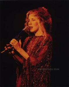 a woman holding a microphone in her right hand and wearing a red dress with sequins on it