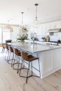 a kitchen with an island and bar stools next to the counter top, along with several lights hanging from the ceiling