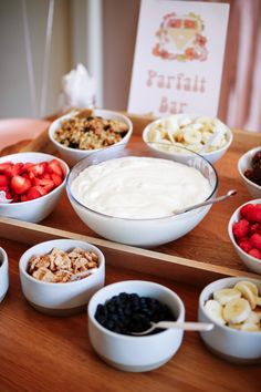 bowls filled with fruit and yogurt sit on a wooden tray next to other dishes