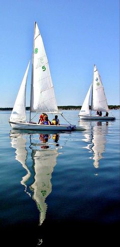 two small sailboats in the water with people on one side and another boat behind them