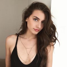 a woman with long brown hair wearing a black tank top and holding a necklace on her neck