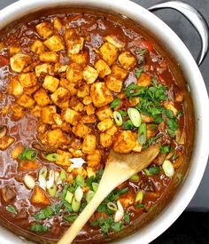 a pot filled with meat and vegetables next to a wooden spoon