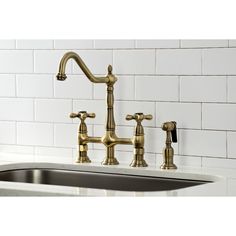 a kitchen sink with two faucets and white tiles on the wall behind it