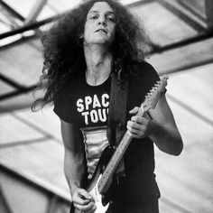 a black and white photo of a man playing an electric guitar with space tour t - shirt on