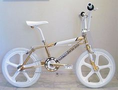 a gold and white bike is parked in front of a wall with a painting on it