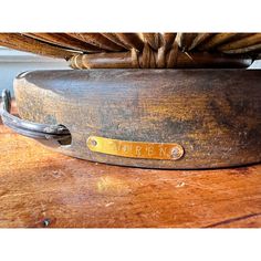 a wooden table with a metal bowl on it and a name plate attached to the top