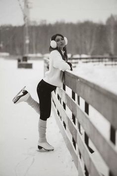 a woman leaning on a fence in the snow wearing headphones and leg warmers