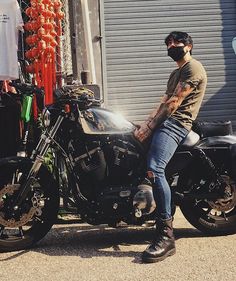 a man sitting on the back of a motorcycle wearing a face mask and looking off into the distance