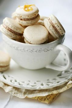 a white cup filled with macaroons on top of a saucer next to cookies