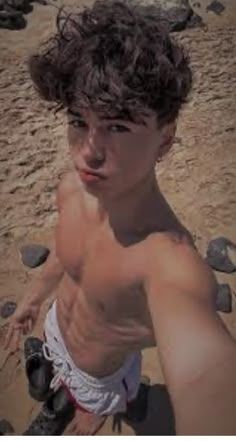 a young man standing on top of a sandy beach next to rocks and holding his arm out