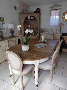 a dining room table with white chairs and flowers in a vase on the top of it