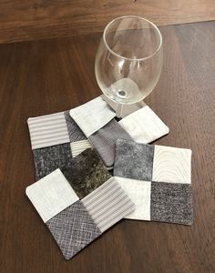 a wine glass sitting on top of a wooden table next to patchwork coasters