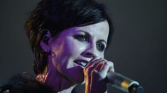 a woman holding a microphone in her right hand and singing into the microphone on stage