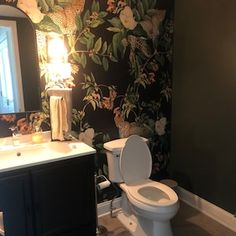 a bathroom with a toilet, sink and mirror next to a wallpapered wall