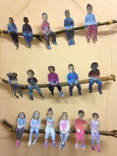 a group of dolls sitting on top of a wooden stick next to each other in front of a wall