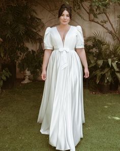 a woman wearing a white dress standing in the grass with her hands on her hips