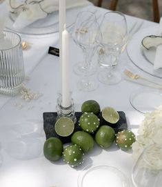 limes and white flowers are on the table with candles, plates and silverware