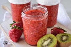 kiwis and strawberries sit on a cutting board next to jars of fruit