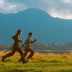 two people running in a field with mountains in the background