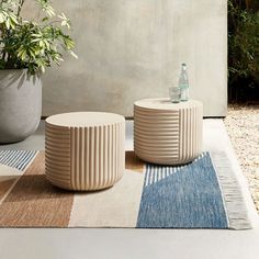 two white tables sitting on top of a rug next to a potted green plant