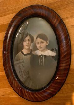 an old photo of two young women in a wooden frame on a wall with wood flooring