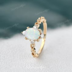 an opal and diamond ring on top of white sand