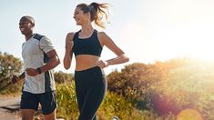 two people running down a dirt road in the sun with trees and bushes behind them