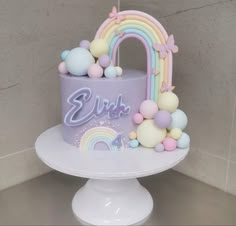 a birthday cake decorated with pastel balloons and a rainbow arch for the top tier