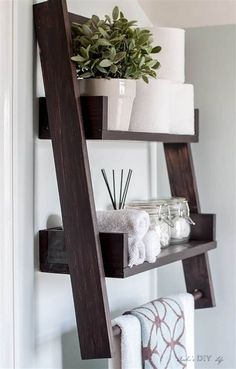 a ladder shelf with towels, candles and plants on it in the corner of a room