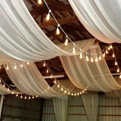 the ceiling is covered with white drapes and string lights hanging from it's sides