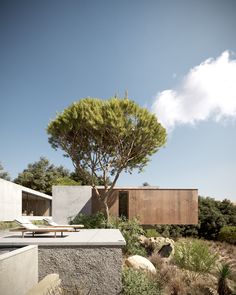 the house is surrounded by trees and rocks, with an outdoor lounge area on one side