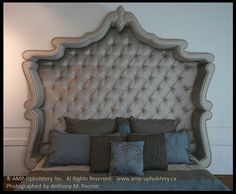 an upholstered headboard and pillows on a bed with white walls in the background