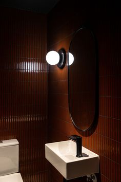 a white toilet sitting next to a bathroom sink under a round mirror on a wall