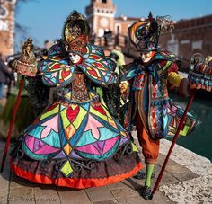 two colorfully dressed people standing next to each other on a brick walkway near water