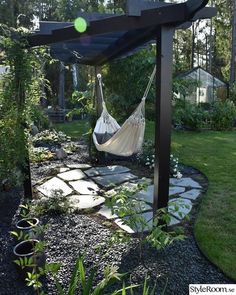 a hammock hanging from a pergolated area in a garden with rocks and grass