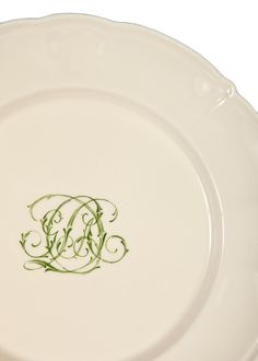 a white plate with green lettering on the bottom and an ornate monogrammed design