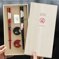 a person holding an open box with various items in it, including pens and chopsticks