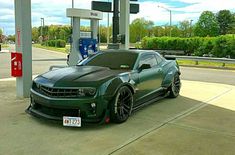 a green chevrolet camaro is parked at a gas station