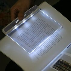 a person is holding an illuminated book in their hand and reading it on the table