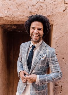 a man wearing a suit and tie standing in front of a building smiling at the camera