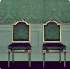 two chairs sitting side by side in front of a wall with green and gold paint