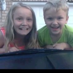 two young children are smiling and posing for the camera in front of a car window