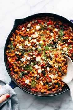 a skillet filled with beans and vegetables on top of a marble countertop next to a wooden spoon