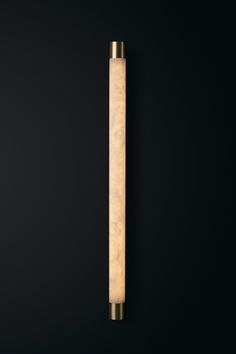 a wall mounted light on the side of a black wall with a gold metal pole