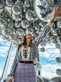 a woman standing in front of a large mirror ball with her hands up to the sky