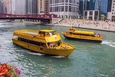 two yellow boats are traveling down the river in front of some tall buildings and bridge