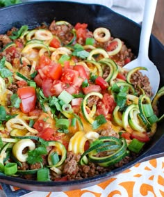 a skillet filled with zucchini, meat and veggies on top of a table